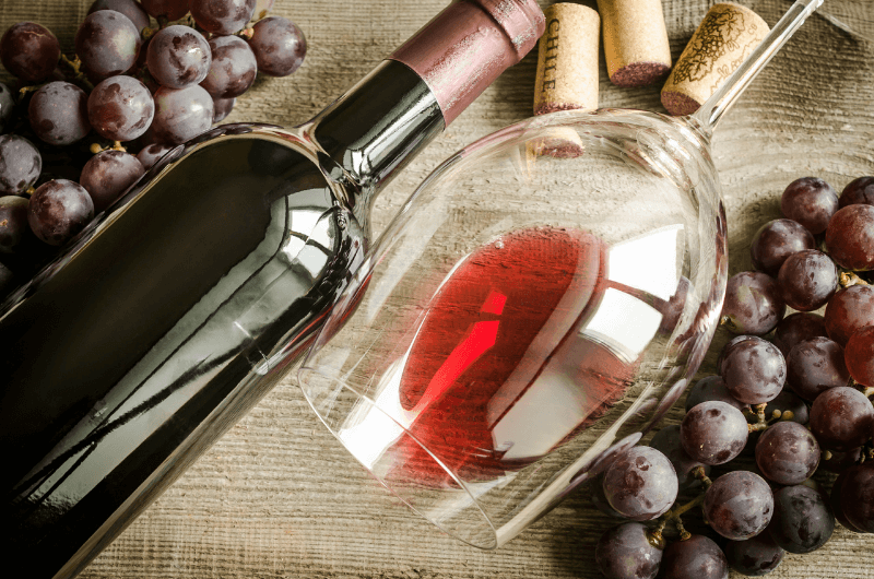 fľaša červeného vína s pohárom s červeným vínom položená na stole